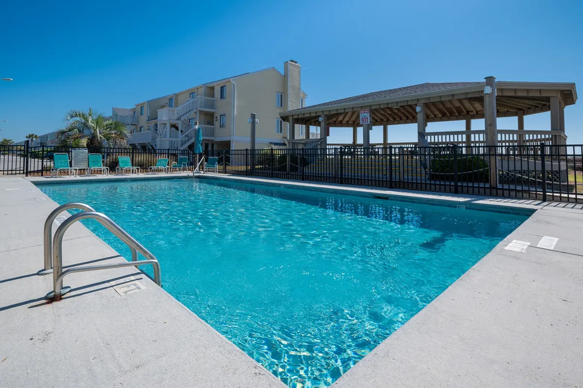 A bright and inviting outdoor pool area surrounded by plenty of lounge chairs and a gazebo. Palm trees add a vacation vibe, while the open layout suggests space for swimming, sunbathing, and socializing. The pool is the focal point, with the gazebo offering a shaded spot for families to relax.