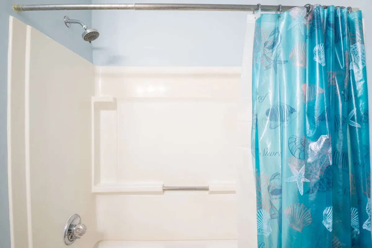 A bright bathroom with a showerhead, a patterned shower curtain, and a bathtub. The space is clean and functional, ideal for morning routines or a soothing bath at the end of the day.