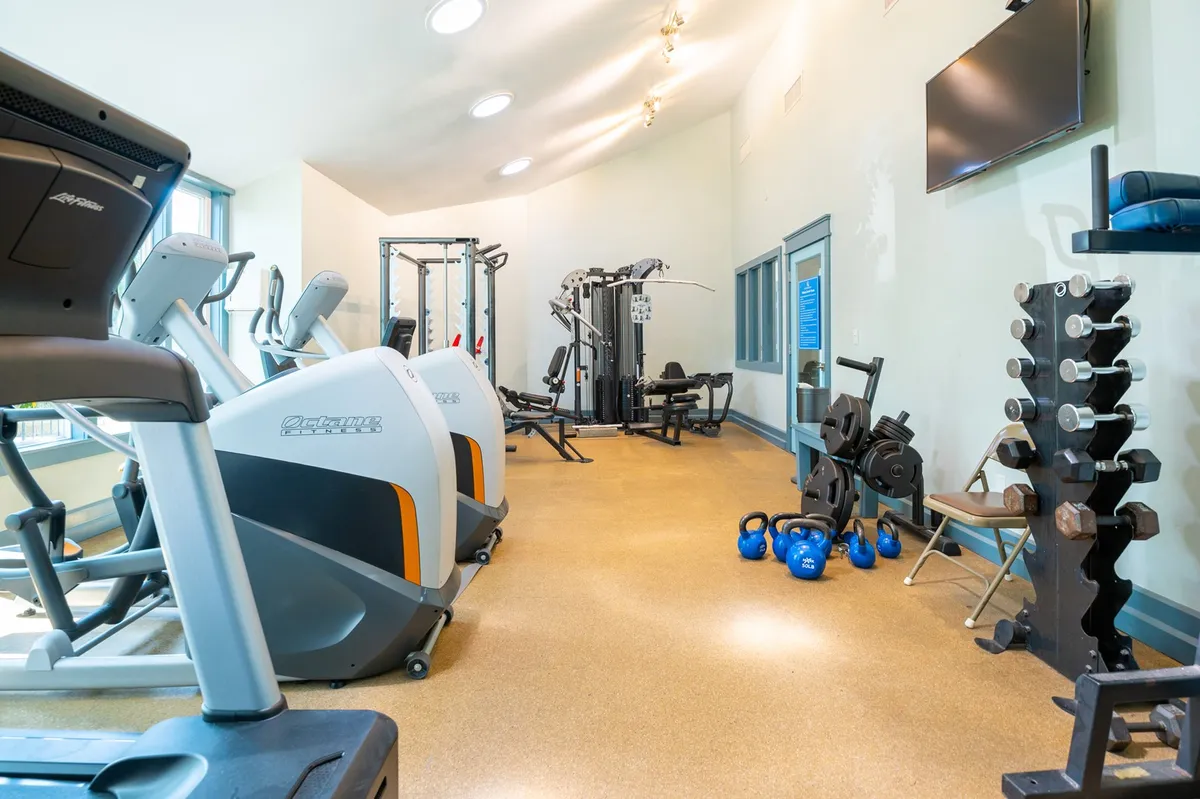 A modern fitness center filled with treadmills, weight machines, free weights, exercise mats, and a TV. The well-lit space is designed for both group workouts and individual exercise, encouraging healthy activity for all guests.