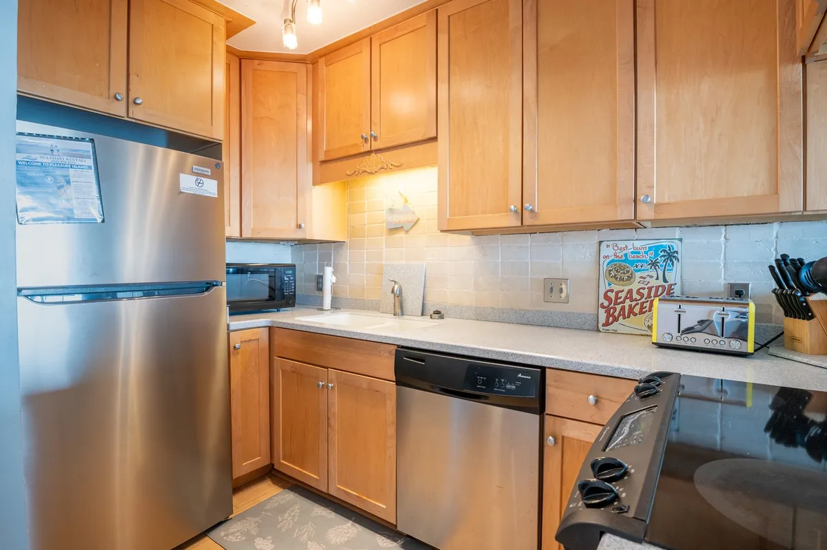 A warm, fully equipped kitchen with stainless steel appliances, wooden cabinets, granite countertops, and a vintage seaside sign. The space is clearly designed for both cooking and gathering, with inviting colors and ample workspace.