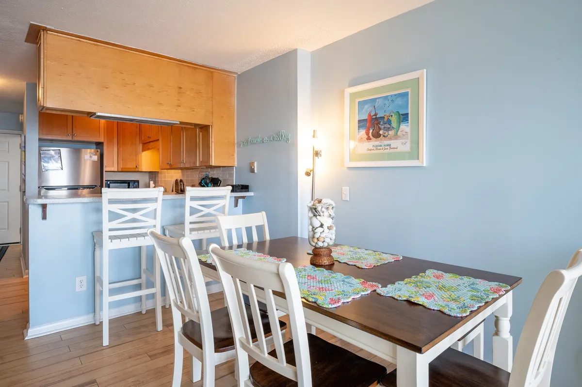 A spacious dining area with a large table set for family meals, adjacent to a modern kitchen. Decorative artwork adds a cheerful touch while ample natural light creates a bright and open environment ideal for gatherings and celebrations.