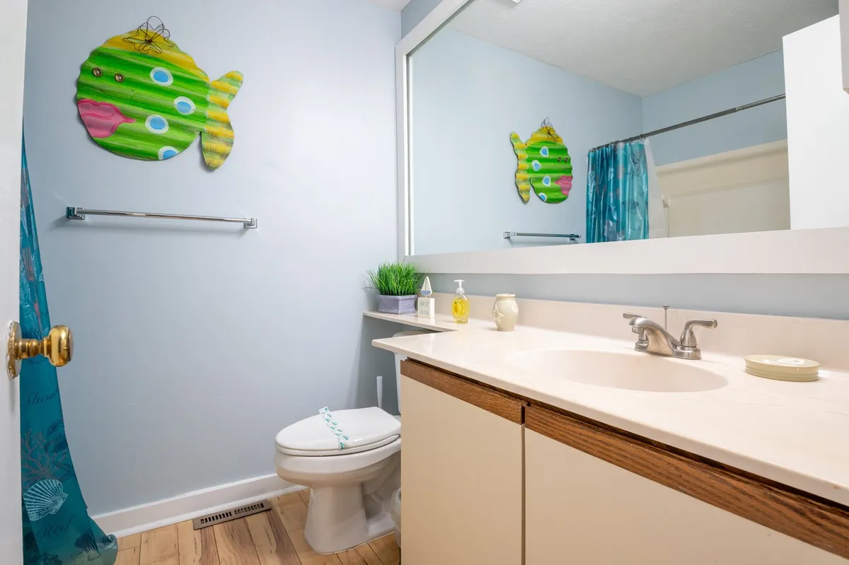 A light-hearted full bathroom with colorful fish wall art, a functional vanity with sink, and a shower curtain. The space is both playful and practical, designed for comfort and ease of use.