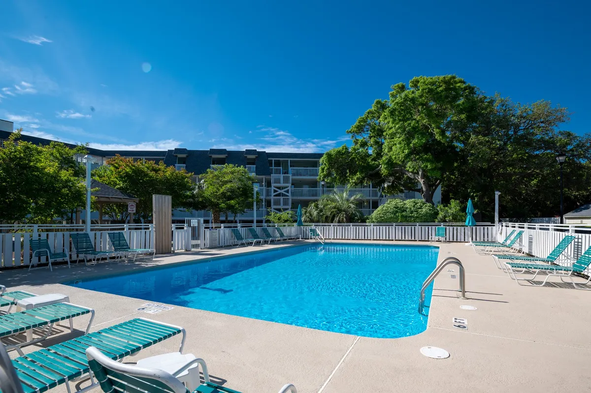 A vibrant exterior scene with a sparkling swimming pool surrounded by lounge chairs, lush greenery, and the building’s façade in the background. The atmosphere is cheerful and relaxed, inviting guests to swim, sunbathe, or socialize by the water, with sunset hues reflecting off the pool.